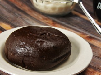 A cup of black coffee, a plate of pastry, and a bowl of sugar on a brown wooden background