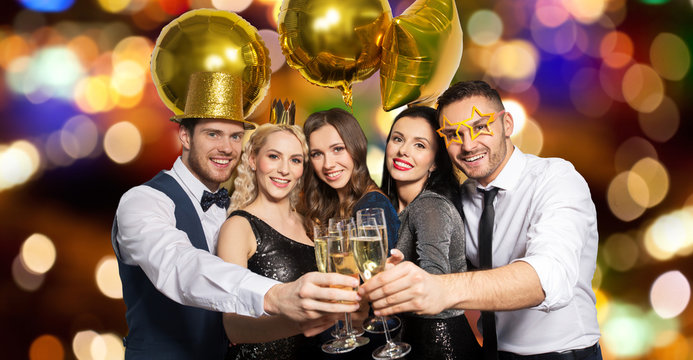 celebration, luxury and holidays concept - happy friends with golden party props clinking champagne glasses over festive lights background