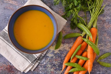 Bowl of vegetable soup surrounded by carrots and peas