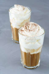 Ice coffee topped with vanilla ice cream, whipped cream and grated chocolate. Gray table, high resolution.