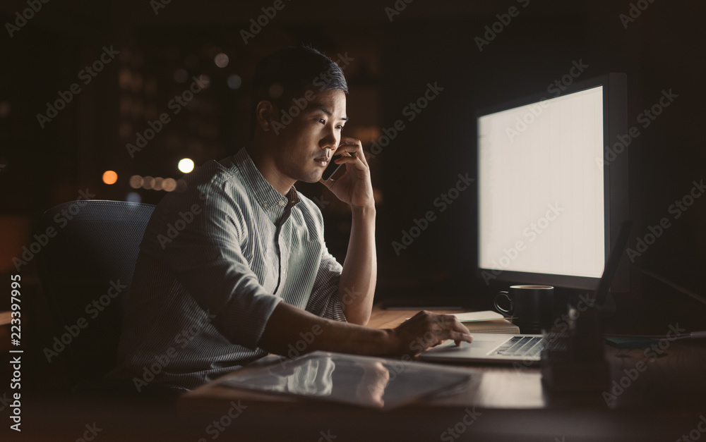 Wall mural asian businessman talking on his cellphone in a dark office