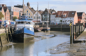 Inner harbor at low tide in the old town of Husum with boats on the mudflat and houses on a sunny...