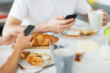 food and technology concept - close up of couple with smartphones having breakfast at home