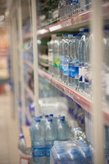 Blurred image of drink water bottles product on shelves in grocery store or supermarket background