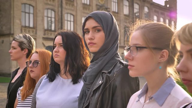 young caucasian woman in hijab directly among of other diverse girls in line outside