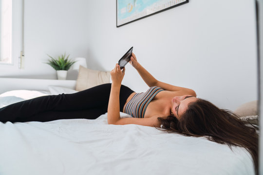 Young woman lying in bed and using mobile phone