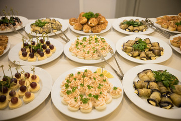 Row of plates with various cold appetizers standing on a table with a white tablecloth