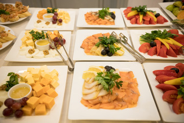 Row of plates with various cold appetizers standing on a table with a white tablecloth