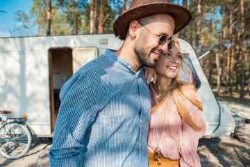 hippie couple embracing near trailer in forest