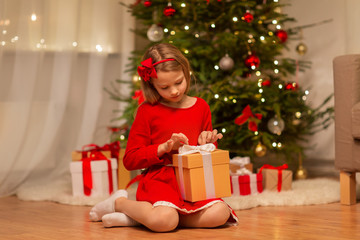 christmas, holidays and childhood concept - girl in red dress with gift box at home