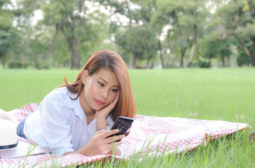 Asian women happy while picnic in the garden,Asian women  enjoy using smartphone while picnic,Asian women happy with Social network in the garden,Selective focus