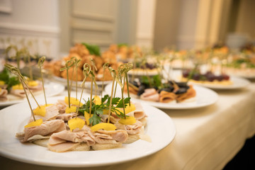 Row of plates with various cold appetizers standing on a table with a white tablecloth