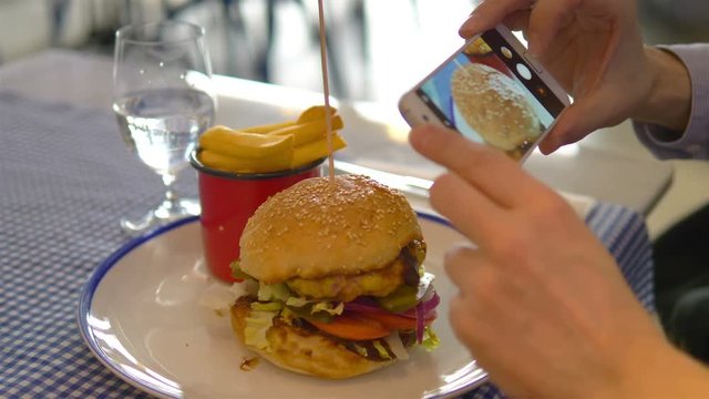 Man taking photos of hamburger by smartphone in 4k slow motion 60fps