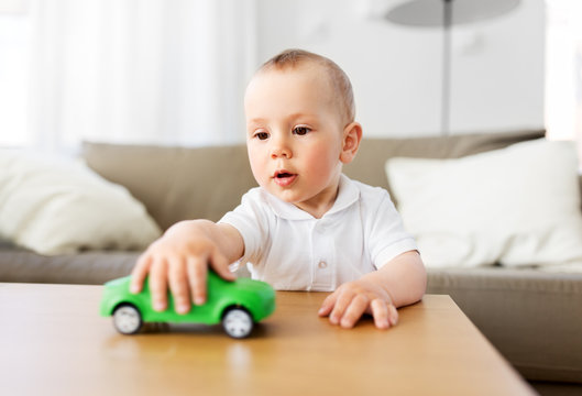 childhood and people concept - baby boy playing with toy car at home