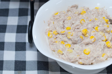 Tuna corn salad cream in white bowl on fabric pattern background