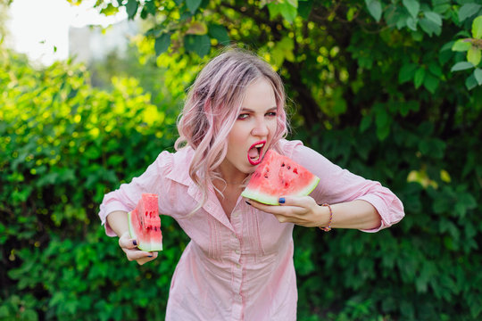 Beautiful young woman with pink hair holding two slices of watermelon