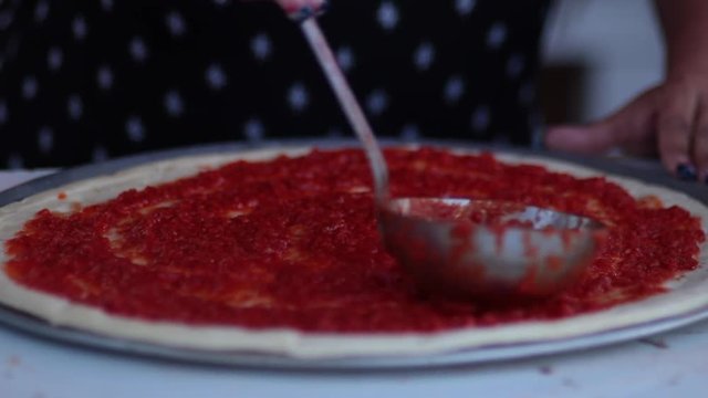 Spreading sauce on pizza dough close up