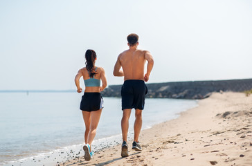fitness, sport and lifestyle concept - happy couple running along summer beach