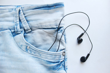 Headphones listen to music from jeans pocket on white background. Playlist concept, youth, fun