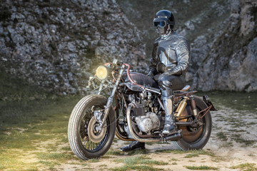 Fototapeta na wymiar Biker with black leather clothes, standing on his custom rat motorcycle in a desolated mountain land. Post apocalyptic concept