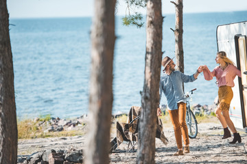 hippie couple holding hands and walking in nature near campervan