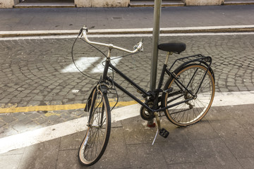 Broken retro bicycle with deflated and damaged wheel, enchained to the light pillar in the street...