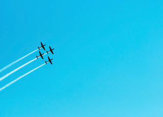 Squad of four airplanes flying together leaving a smoke trail behind. Aerial acrobatics airplanes. Clear blue sky day. Large space for text on sky.