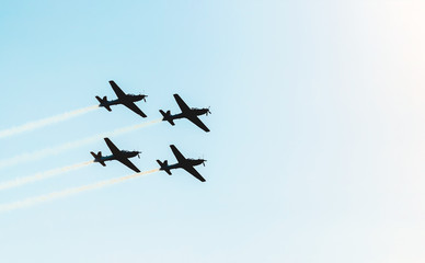 Silhouette of a squad of four airplanes flying together leaving a smoke trail behind. Aerial acrobatics airplanes. Space for text on sky.