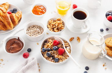 Obraz na płótnie Canvas healthy breakfast with granola, berry, nuts, croissant, jam, chocolate spread and coffee
