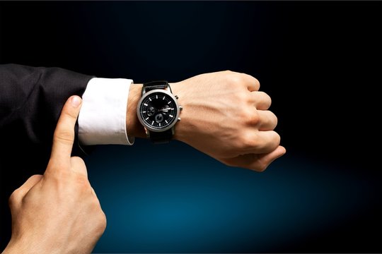 Businessman pointing at hand watch on grey wall background