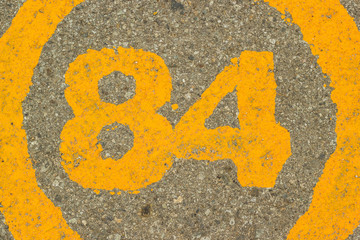 The number 84 embedded in asphalt concrete.