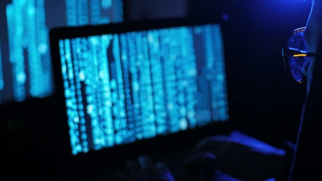 Young cyberpunk student hacker typing on the computed under the blue neon light.