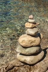 Fototapeta na wymiar Pile of pebbles on the sea front on a beautiful day. Pebble stack on the seashore. Stone pyramid. Balanced Zen stones.