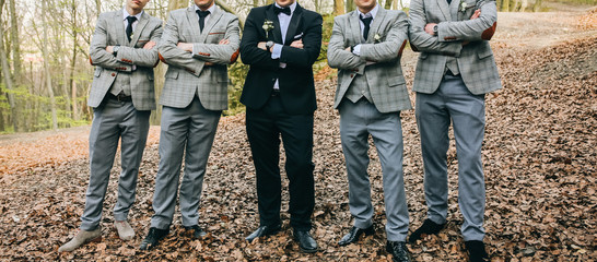 Groom is standing with his friends in the autumn wood. Best man in stylish elegant checkered suits. Groomsmen at wedding photoshoot.