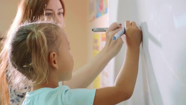 Little cute girl with teacher writing on the blackboard in classroom