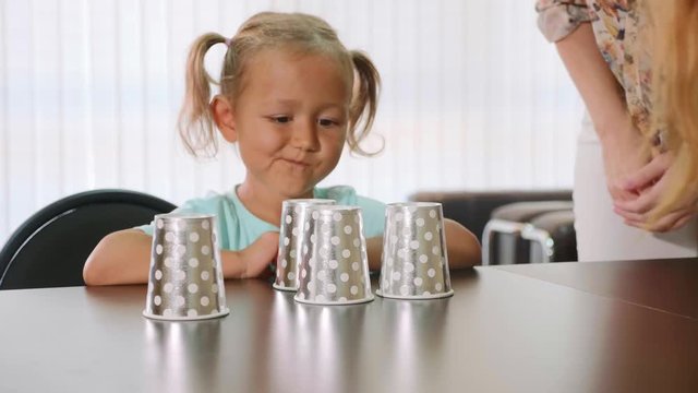 Psychologist testing little child girl during shell game with cups