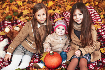 Three happy little sisters having fun playing with fallen golden leaves