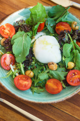 Mozzarella with cherry tomatoes with arugula and olives in a plate on a wooden table. 