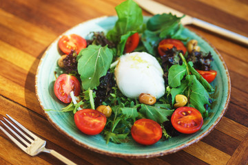 Mozzarella with cherry tomatoes with arugula and olives in a plate on a wooden table. 