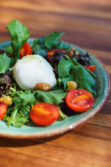 Mozzarella with cherry tomatoes with arugula and olives in a plate on a wooden table. 