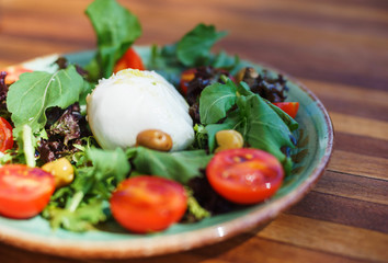 Mozzarella with cherry tomatoes with arugula and olives in a plate on a wooden table. 