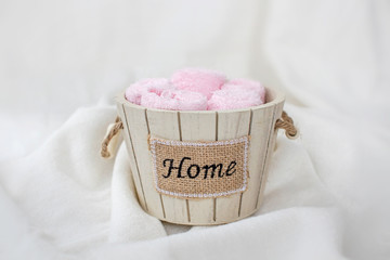 Set of pink towels in a wooden decorative bucket with the inscription " home" on a soft white background