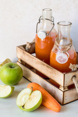 Fresh carrots and apples, next to a wooden box with two glass bottles of natural homemade juice. The concept of healthy eating.