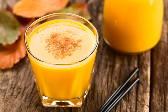 Fresh homemade pumpkin smoothie with cinnamon in glass, drinking straws on the side, photographed on wood (Selective Focus, Focus one third into the top of the drink)