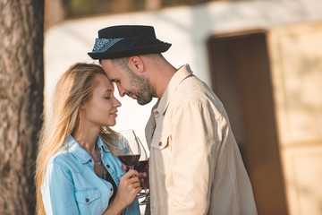 young couple touching the foreheads and holding glasses of wine near trailer