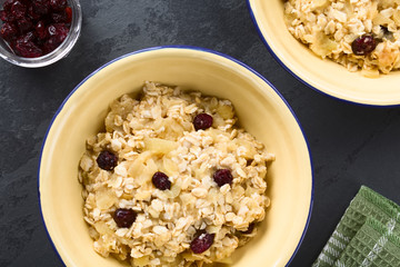Fresh homemade vegan cooked apple, oatmeal, cranberry and cinnamon porridge, served in bowls, photographed overhead on slate (Selective Focus, Focus on the porridge)