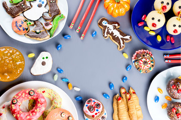 Halloween sweet treats, party food concept. Scary cookies, monster biscuits and fruits on grey background.