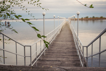 Fototapeta premium Perspective view of a wooden pier on the pond at sunset with seagulls