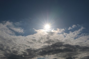 Naklejka na ściany i meble sun is shining behind white clouds at the blue sky