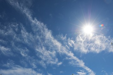 Naklejka na ściany i meble sun is shining behind white clouds at the blue sky